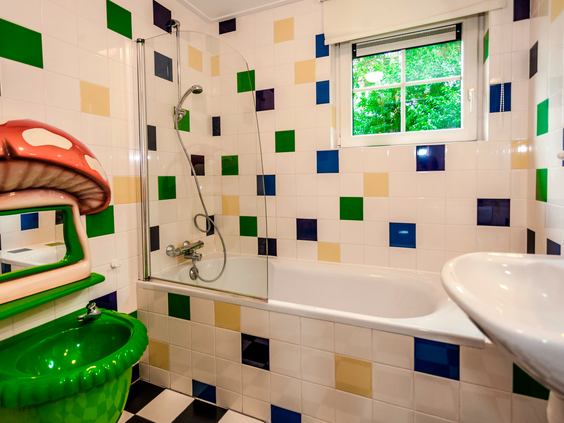 Een vrolijke badkamer in een kinderbungalow met kleurrijke tegels, een bad en een speciale kindvriendelijke wastafel in de vorm van een paddenstoel.