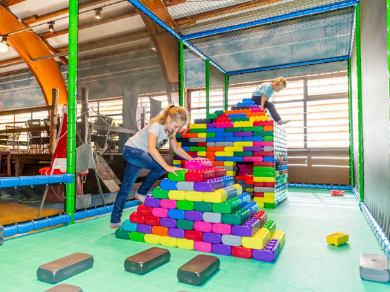 Kinderen bouwen een hoge toren met grote, gekleurde speelblokken in het indoorspeelparadijs van Landal Hochwald.