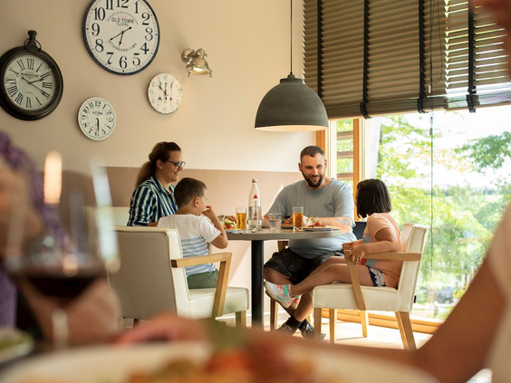 Een familie met twee kinderen zit gezellig te eten en te praten aan een tafel in het parkrestaurant van Landal Hochwald.