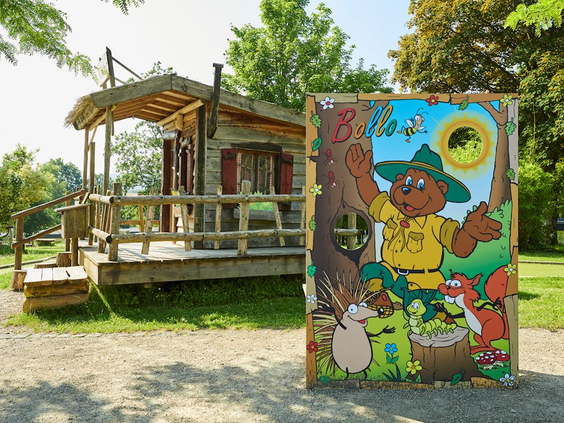 De ingang van een houten speelhuisje van de Bollo Club, met daarnaast een vrolijk bord met een tekening van Bollo de Beer.