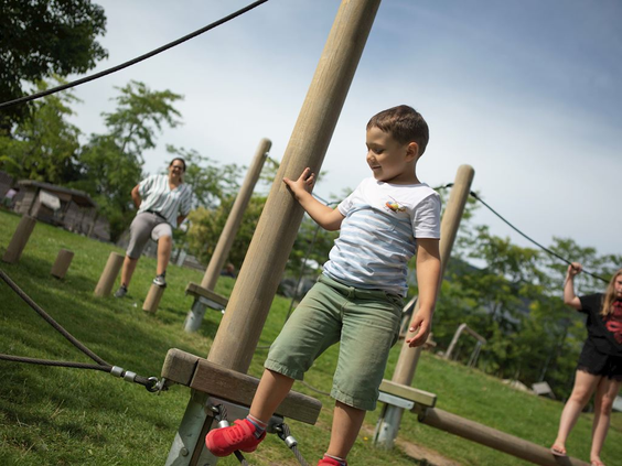 Een jongen balanceert behendig over een laag touwenparcours met houten obstakels in de buitenspeeltuin van Landal Hochwald.