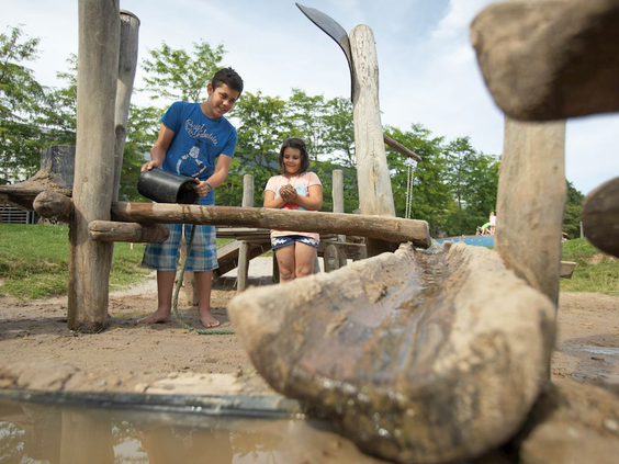 Kinderen spelen met zand en water bij de houten watergoten en pompen van de waterspeelplaats op Landal Hochwald.