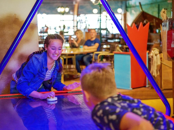 Kinderen spelen fanatiek een potje airhockey op een oplichtende speeltafel in de recreatieruimte van Landal Hochwald.