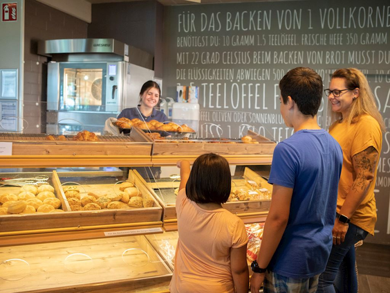 Een gezin koopt verse broodjes en lekkernijen in de bakkerij van de parkshop op Landal Hochwald.