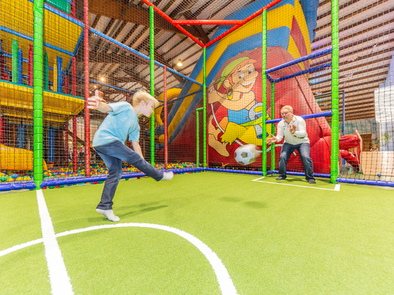 Twee jongens voetballen op het sportveldje in het kleurrijke indoorspeelparadijs van Landal Hochwald.