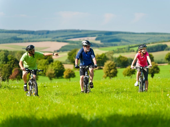 Een familie met kinderen fietst door het groene, heuvelachtige landschap in de omgeving van Landal Hochwald.
