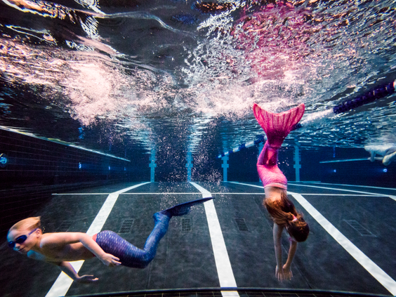 Twee kinderen met zeemeerminstaarten zwemmen onder water in het zwembad van Landal Hof van Saksen tijdens de workshop zeemeerminzwemmen.