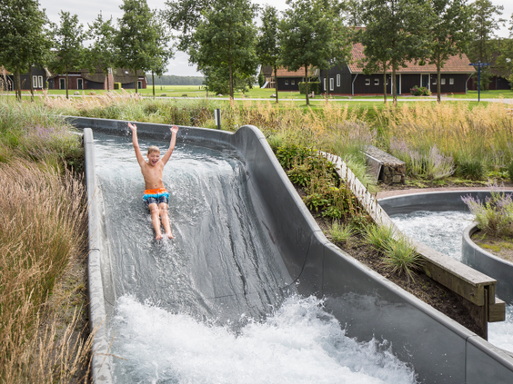 Een jongen met zijn armen in de lucht glijdt van een brede waterglijbaan in het buitengedeelte van het zwemparadijs van Landal Hof van Saksen.