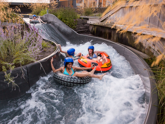 Drie kinderen met helm op zitten samen in een grote opblaasbare band en glijden door de wildwaterbaan, één van de spectaculaire glijbanen van Landal Hof van Saksen.