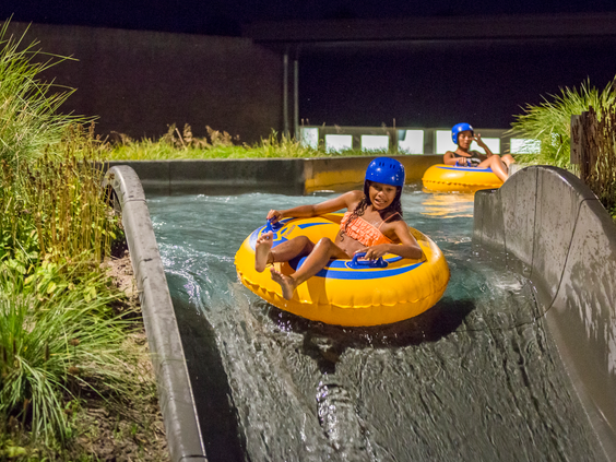 Twee kinderen met helmen op varen in gele opblaasbare banden door de wildwaterbaan van Landal Hof van Saksen in de avond.