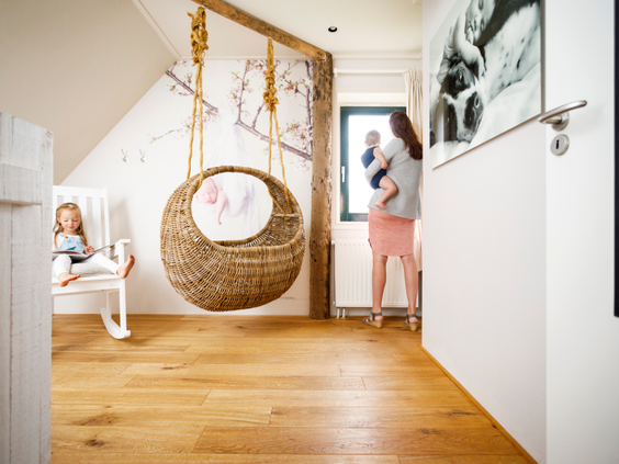 Het stijlvolle interieur van de Newborn-boerderij op Landal Hof van Saksen, met een moeder die haar baby vasthoudt in een kamer met een hangstoel en een schommelstoel.