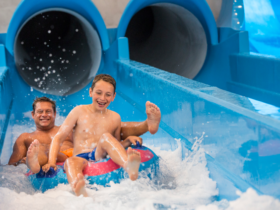 Een lachende vader en zoon zitten samen in een tweepersoonsband en maken een grote plons aan het einde van een waterglijbaan bij Landal Hof van Saksen.