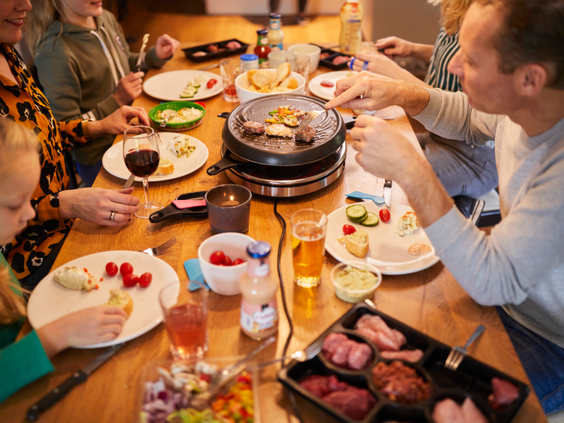 Een gezin zit gezellig aan een houten eettafel te gourmetten in hun sfeervolle Saksische boerderij op Landal Hof van Saksen.