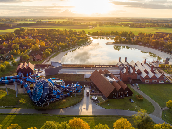 Een luchtfoto van vakantieresort Landal Hof van Saksen bij zonsondergang, met een duidelijk overzicht van de Havezate, de enorme waterglijbanen en het grote recreatiemeer.