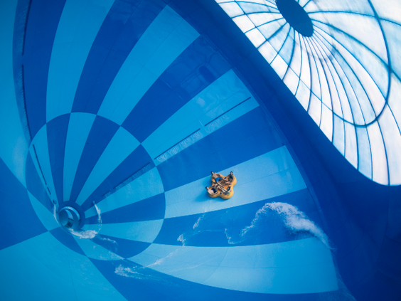 Een groep mensen in een gele opblaasbare band glijdt door de gigantische, blauw-wit geblokte trechter van de waterglijbaan Saltato in het zwemparadijs van Landal Hof van Saksen.