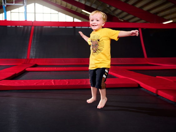 Een blije, jonge jongen in een geel t-shirt springt met zijn armen wijd op een grote trampoline in de Bounz® Arena van Landal Hof van Saksen.