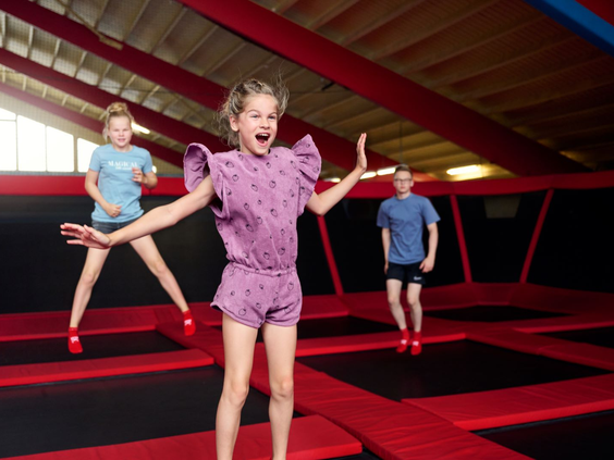 Drie lachende kinderen springen tegelijk in de lucht op de aaneengesloten trampolines van de grote Bounz® Arena bij Landal Hof van Saksen.