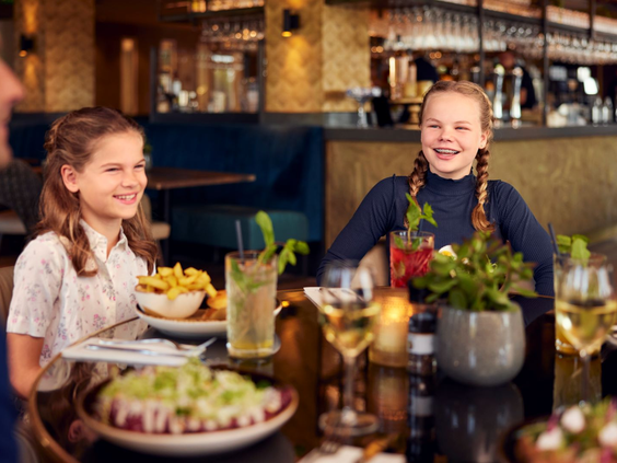 Twee lachende meisjes zitten aan een gedekte tafel met borden eten en drinken in het sfeervolle Italiaanse restaurant Gusto op Landal Hof van Saksen.