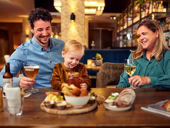 Een jong gezin, bestaande uit vader, moeder en een zoontje, geniet van een drankje en een borrelplank in het sfeervolle Grand Café van Landal Hof van Saksen.