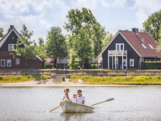 Een gezin met twee kinderen geniet van een boottochtje in een roeiboot op het recreatiemeer van Landal Hof van Saksen, met de Saksische boerderijen op de achtergrond.