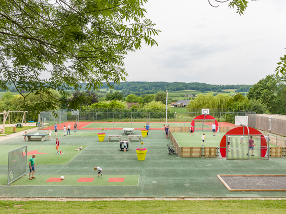 Kinderen spelen en sporten op het grote, multifunctionele sportveld met uitzicht op het heuvelachtige landschap van Limburg.