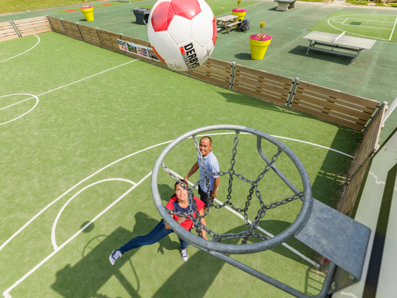 Een man en vrouw spelen een balspel op het sportveld, waarbij ze een enorme bal door een grote ring proberen te gooien op Landal Hoog Vaals.