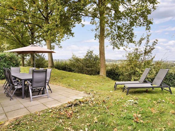 De privétuin van een vakantiehuis met een gemeubileerd terras, twee ligbedden om te zonnen en uitzicht op de groene omgeving.