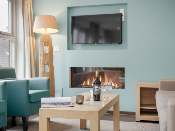 De sfeervolle woonkamer van een vakantiehuis op Landal Hoog Vaals, met een comfortabele zithoek en een gezellige sfeerhaard.