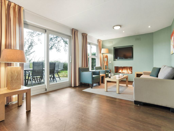 Het ruime en lichte interieur van de woonkamer in een vakantiehuis, met een zithoek, sfeerhaard en openslaande deuren naar het terras.