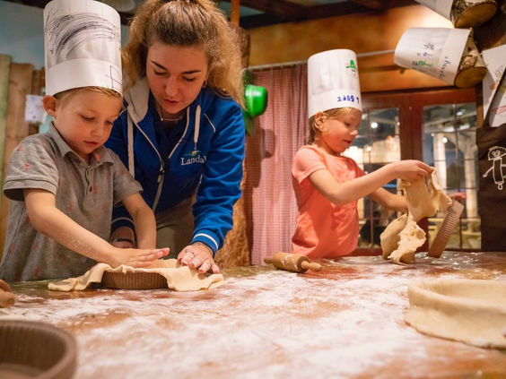 Twee jonge kinderen met koksmutsen op zijn deeg aan het kneden onder begeleiding van het animatieteam op Landal Hoog Vaals.