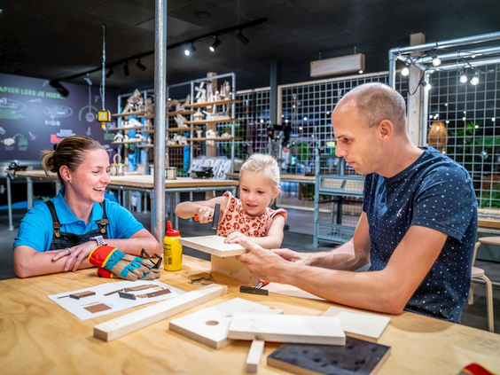 Een gezin is samen een houten vogelhuisje aan het bouwen aan een werktafel in de knutselwerkplaats van Landal Hoog Vaals.
