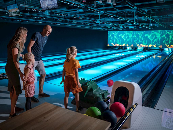 Een gezin met twee kinderen staat klaar om te gooien op de sfeervolle bowlingbaan met blauwe ledverlichting op Landal Hoog Vaals.