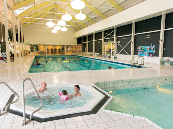 Een gezin met een jong kind ontspant in de warme whirlpool naast het grote overdekte zwembad van Landal Hoog Vaals.