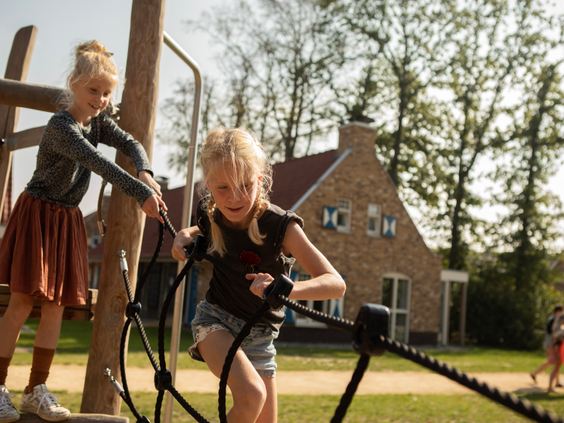 Twee meisjes klimmen en klauteren op een avontuurlijk touwenparcours in de speeltuin van Landal Kaatsheuvel.