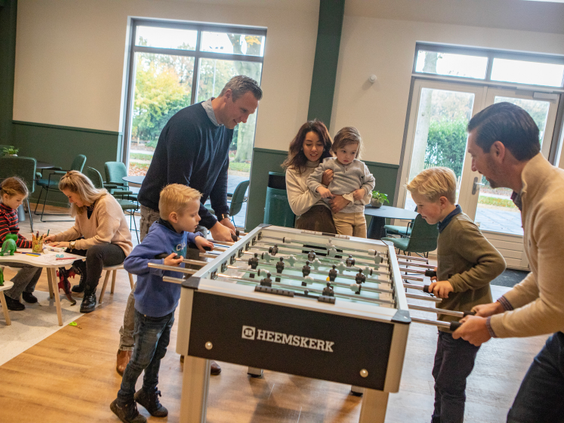 Kinderen en volwassenen spelen samen fanatiek een potje tafelvoetbal in de indoor speelruimte van Landal Kaatsheuvel.