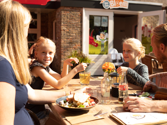 Een gezin met twee dochters geniet van een lunch op het zonnige terras van restaurant Bistro De Bloem op vakantiepark Landal Kaatsheuvel.