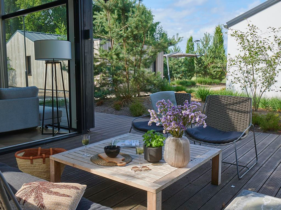 Een ruim en gezellig houten terras bij een vakantiewoning op Landal Klein Oisterwijk, omgeven door groene planten en bomen, met een comfortabele loungeset.