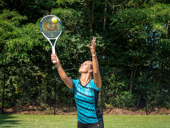 Een jongen serveert met een tennisracket op de outdoor tennisbaan van Landal Marina Resort Well.