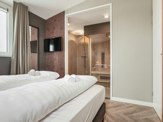 Luxe slaapkamer met een opgemaakt tweepersoonsbed en een moderne en-suite badkamer met glazen wand in een woning op Landal Marina Resort Well.