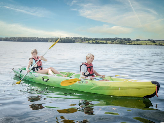 Twee kinderen met zwemvesten aan die samen in een kayak peddelen op het Leukermeer bij Landal Marina Resort Well.