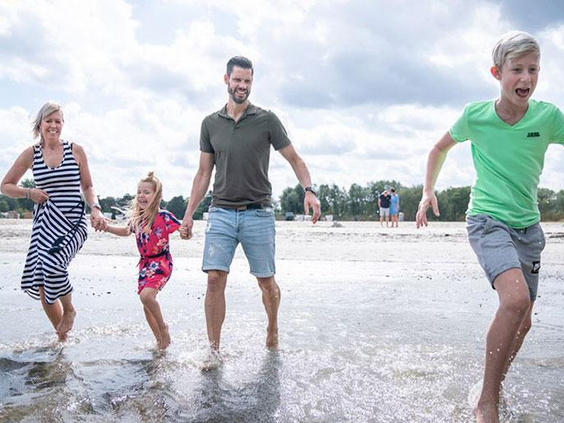 Lachende familie met kinderen spettert en speelt in het ondiepe water bij Landal Marissa, genietend van strand en meer.