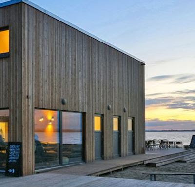Stijlvolle moderne vakantiewoning van Landal Marissa aan het water tijdens zonsondergang, met sfeervolle verlichting en houten gevel.