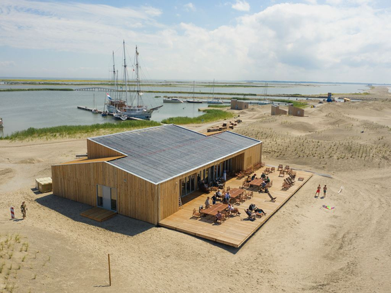 Luchtfoto van het Eilandpaviljoen op Landal Marker Wadden, met een zonnig terras en zicht op de zeilboot in de haven.