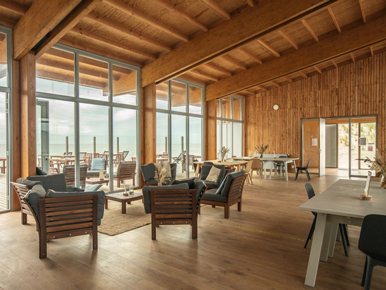 De ruime, houten lounge van het Eilandpaviljoen op Landal Marker Wadden, met comfortabele zithoeken en een hoog plafond.