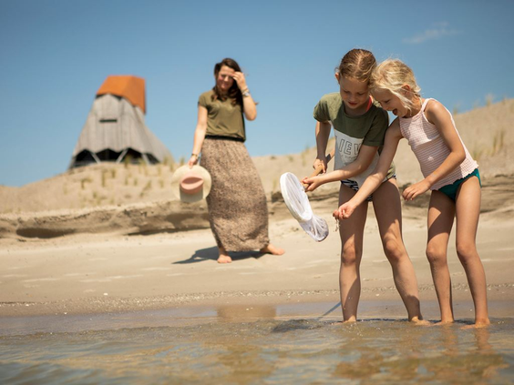 Een moeder en twee kinderen zoeken met een schepnetje naar waterdiertjes en schelpen in het ondiepe water aan het strand van de Marker Wadden.