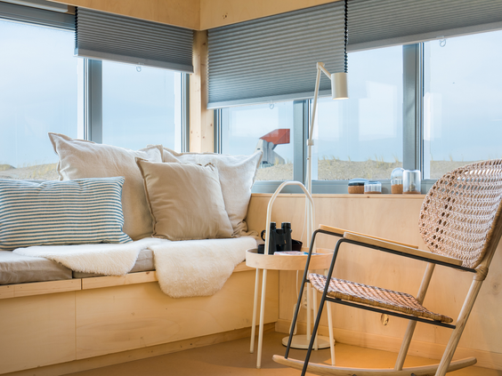 Het lichte, duurzame interieur van een eilandhuisje op Landal Marker Wadden, met een gezellige zithoek bij het raam en een verrekijker.