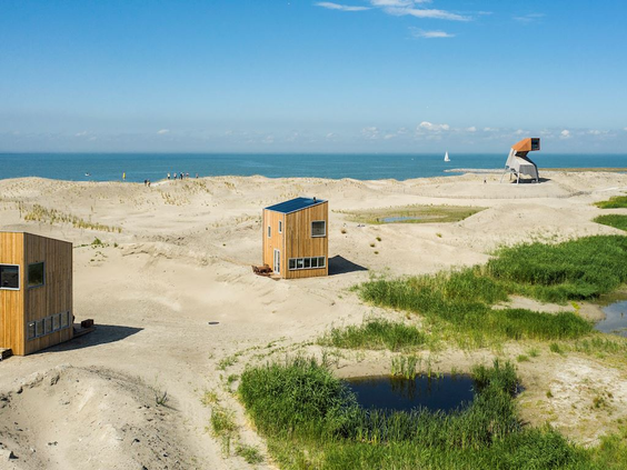 Houten vogelkijkhutten verspreid over het uitgestrekte zandstrand van de Marker Wadden, met het Markermeer op de achtergrond.