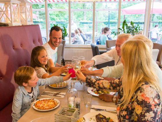 Familie met opa en oma proost tijdens een gezellig diner in het restaurant van Landal Miggelenberg.