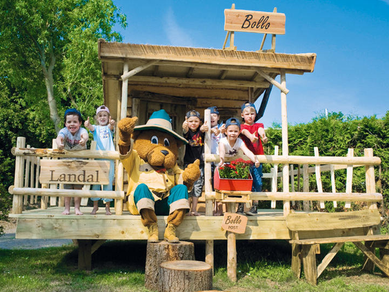 Kinderen poseren vrolijk met Bollo de Beer, de mascotte van Landal, op de veranda van de Bollo Club.