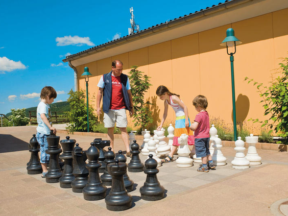 Een vader speelt samen met zijn kinderen met het reusachtige buitenschaakspel op het terras van Landal Mont Royal.